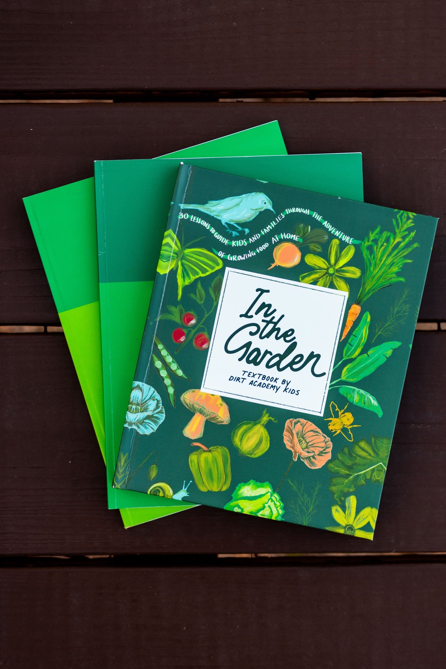 Three green notebooks with garden-themed designs on a wooden surface